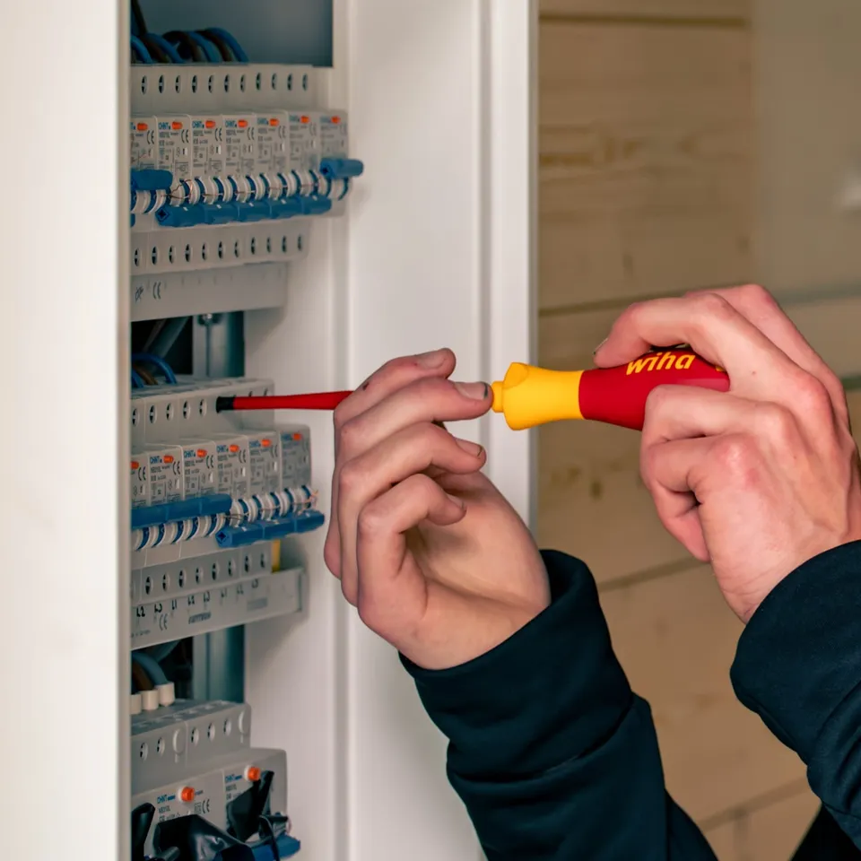 Elektriker kontrollerer sikringer i et sikringsskap med skrutrekker